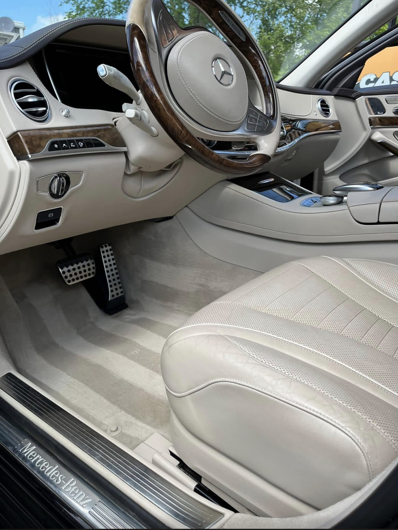Cream leather interior of a Mercedes-Benz with wood-trimmed steering wheel and clean carpet