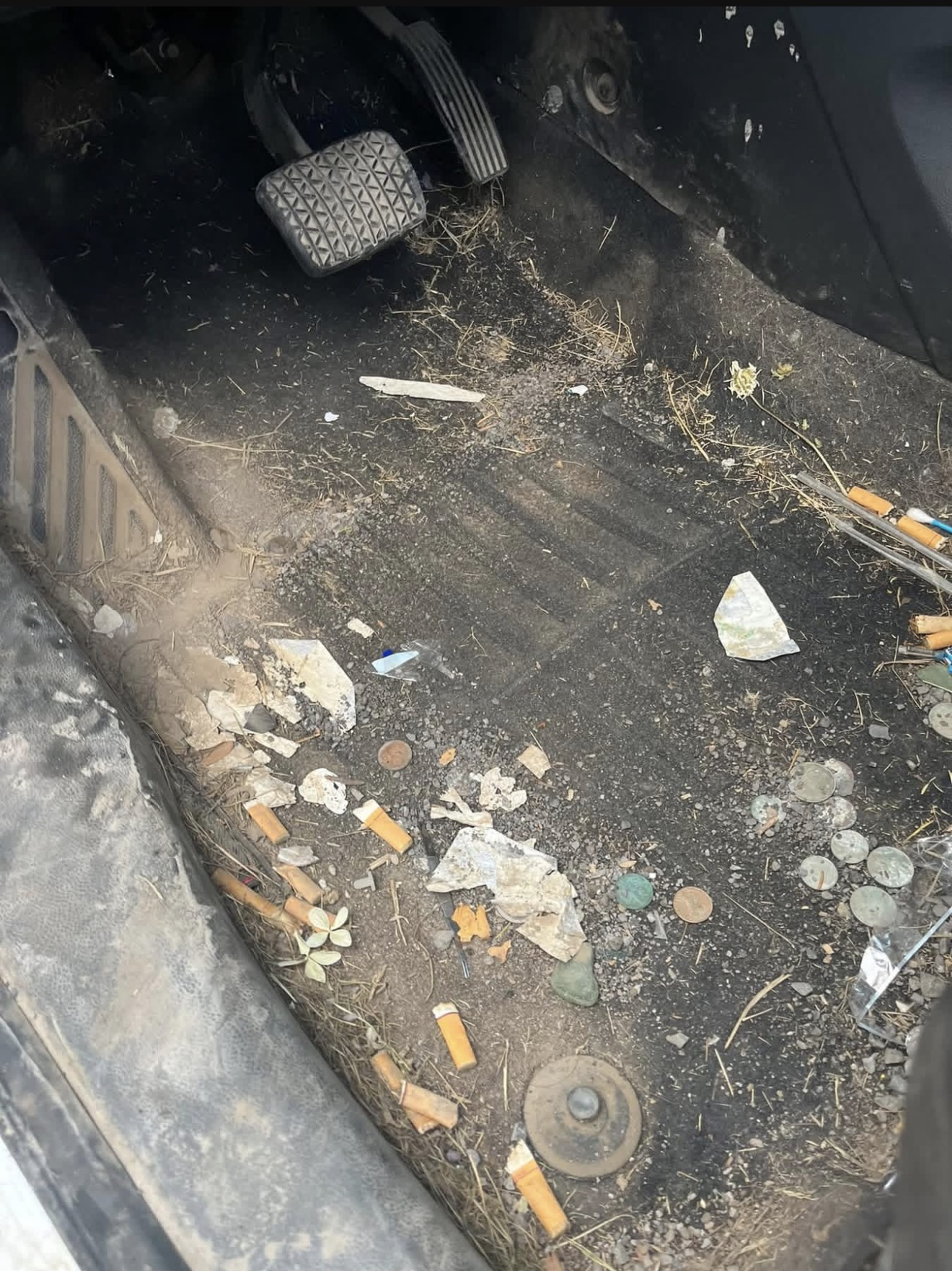 Dirty car floor littered with cigarette butts, coins, debris and dried grass